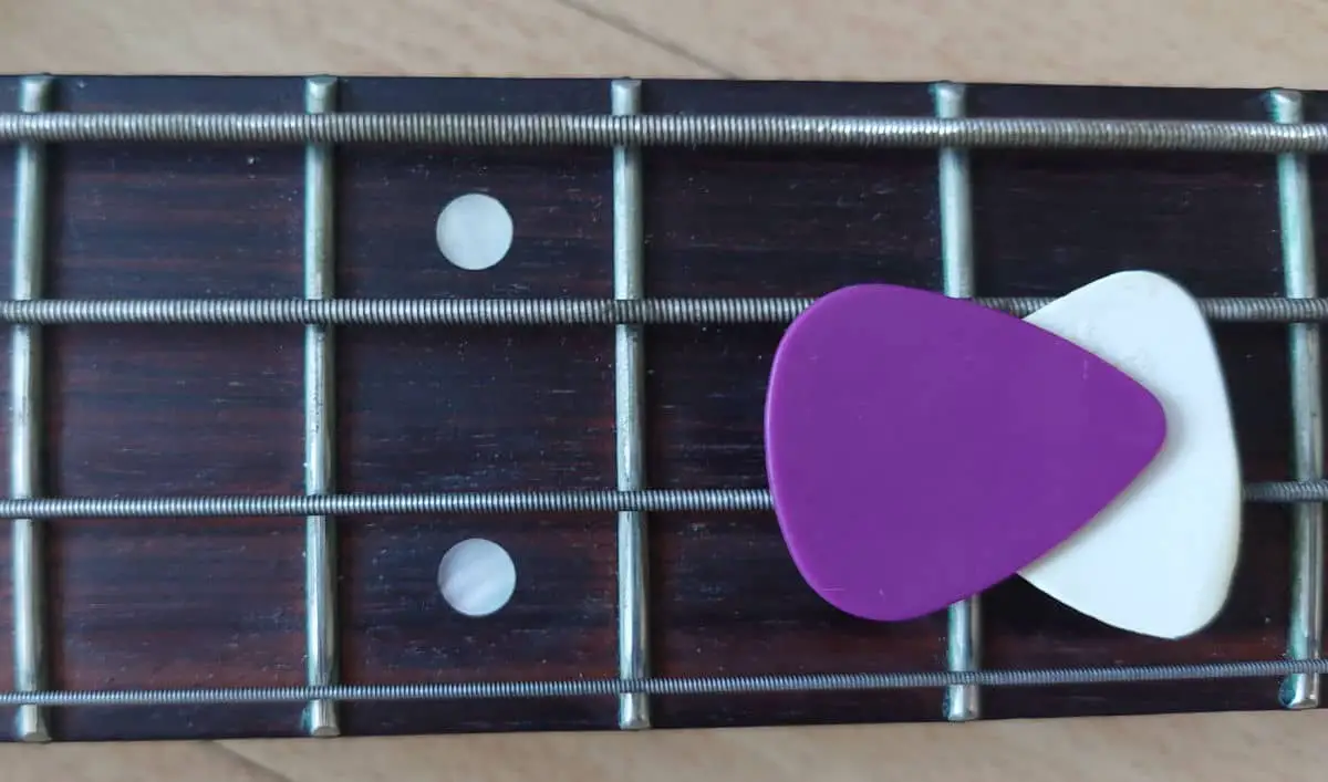 bass pick and guitar pick laying on top of bass guitar