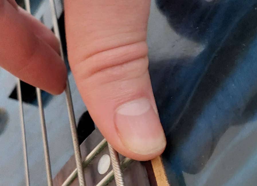 thumb resting on the neck of bass guitar