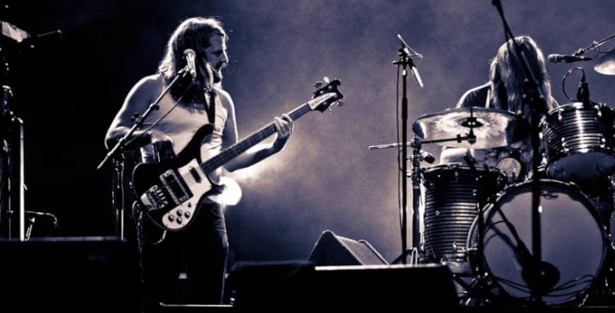 bassist playing rickenbacker bass looking over at drummer during live gig